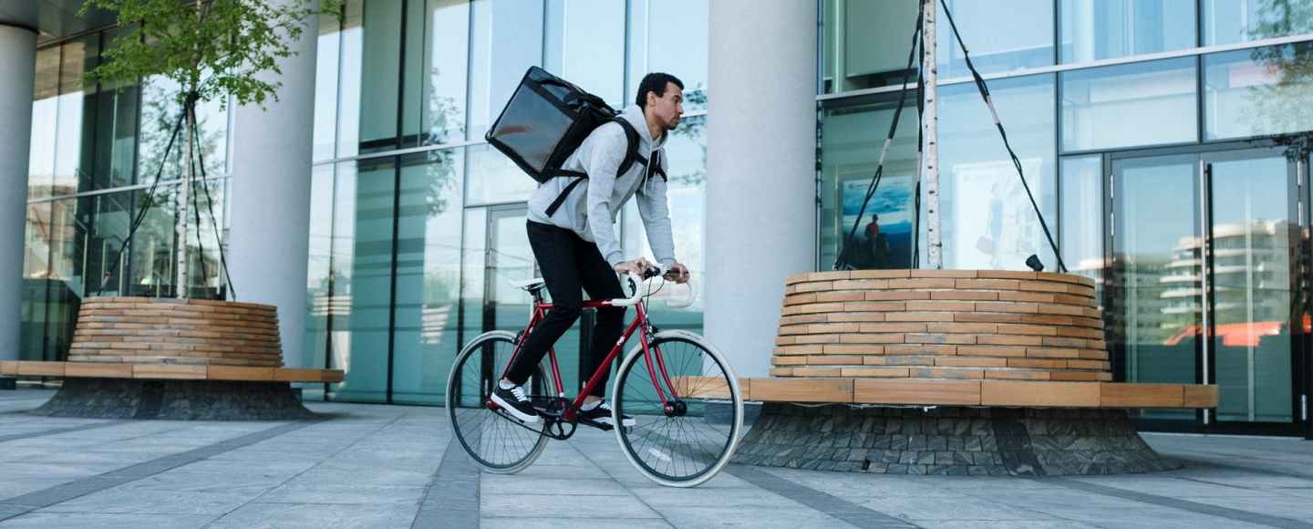Man in white long sleeve shirt and blue denim jeans riding on black city bike working for Ubereats