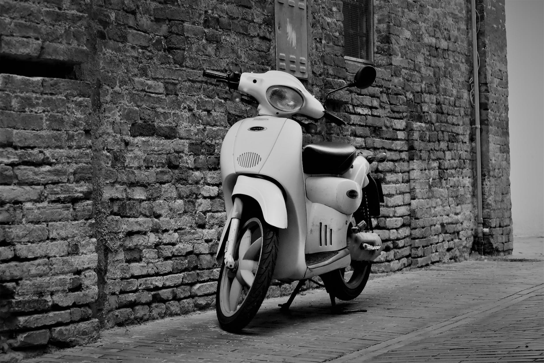 White 50cc moped parked on its stand next to a wall